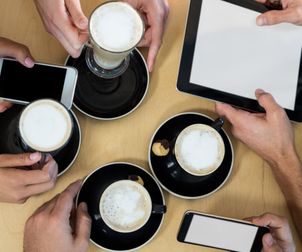 Friends using mobile phone and digital tablet while having cup of coff